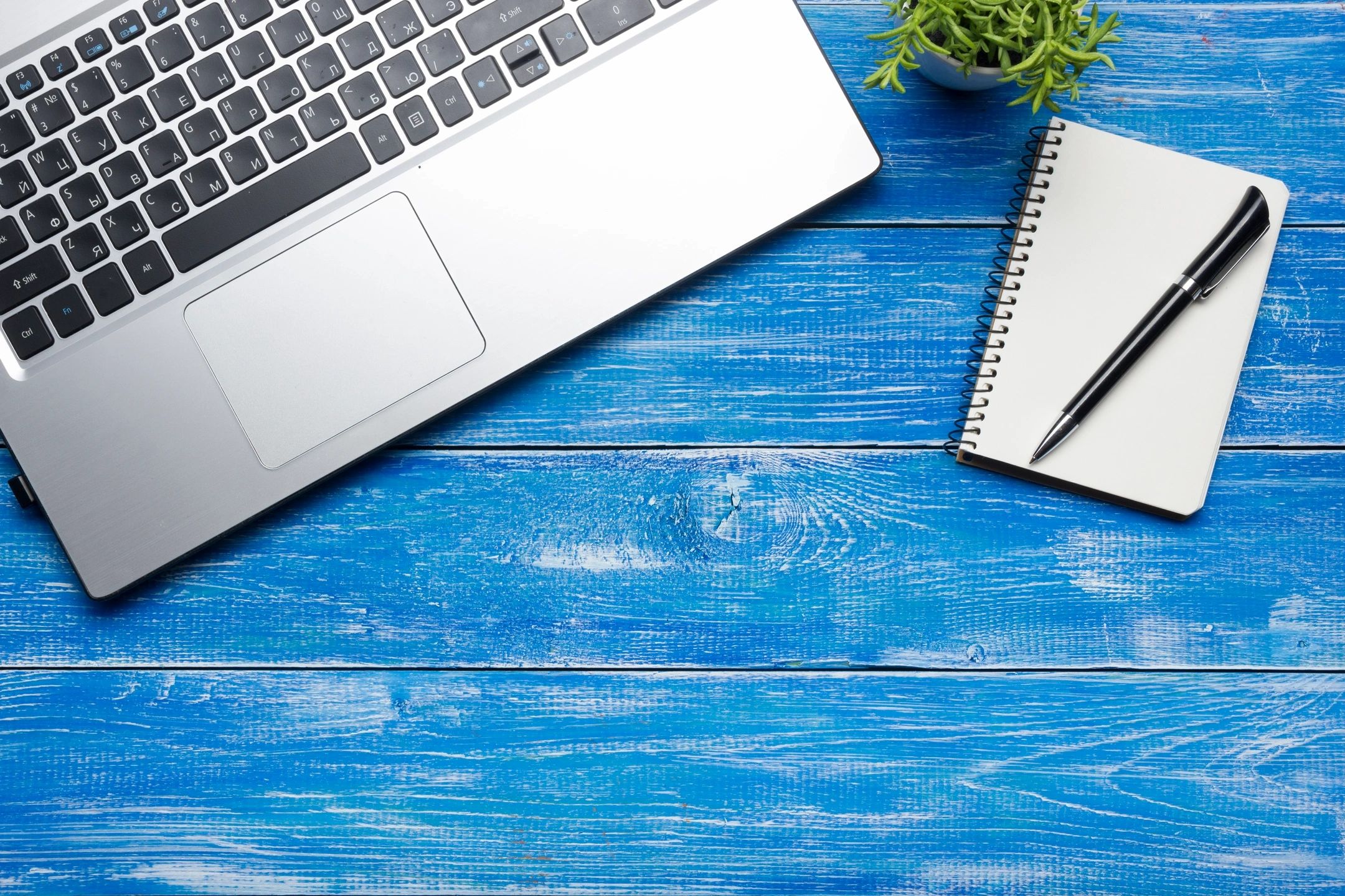 A laptop and a pad with pen on a blue wooden table